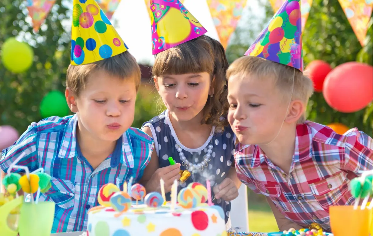 Three children blowing out candles on a birthday cake.